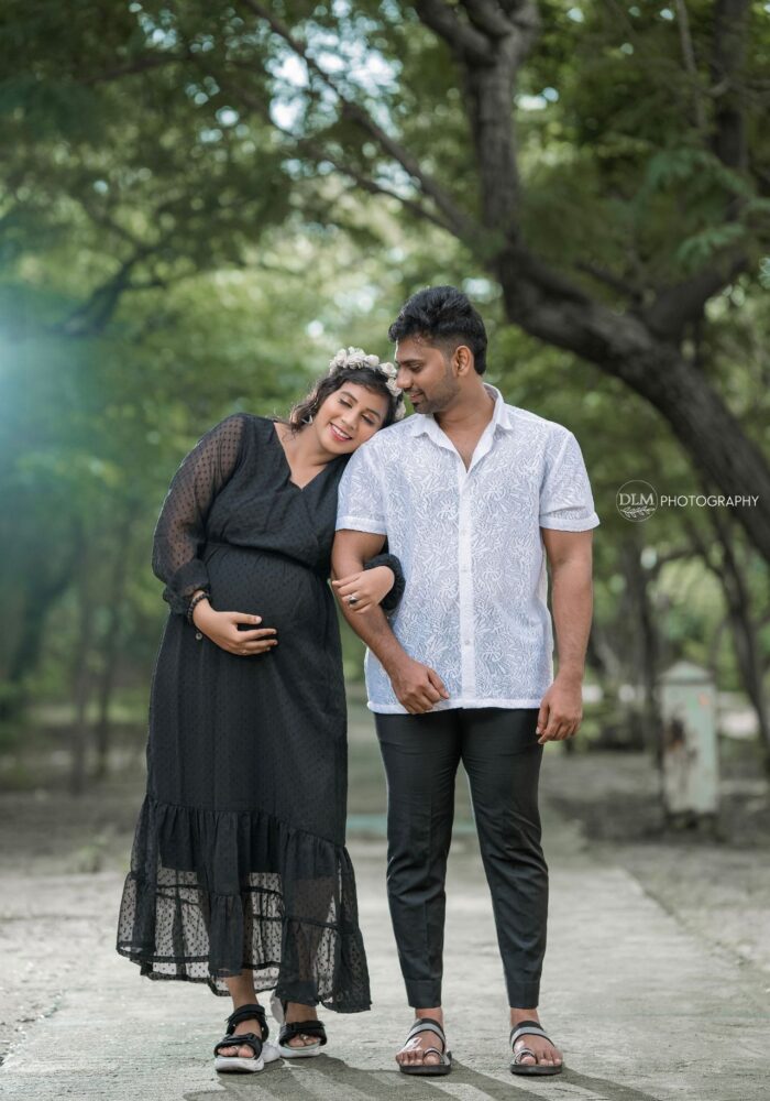 Indian couple posing for maternity baby shoot. The couple is posing in a  lawn with green grass and the woman is falunting her baby bump in Lodhi  Garden in New Delhi, India